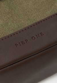 Brown leather and green textured fabric, with embossed "PIER ONE" logo. Smooth finishes and stitching details visible.