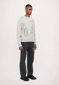 Grå sweatshirt med texturerad grafisk design, rund hals och ribbad mudd. Kombinerad med löst sittande svarta byxor med färgad logotyp. Svarta skor.