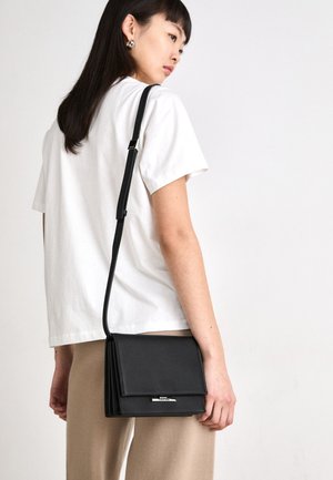 Borsa a tracolla nera in pelle con un design strutturato, accessori in argento e un pattina pieghevole. La tracolla è regolabile per lunghezze diverse.