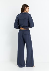Marineblaues, leicht verkürztes Top mit fransigen Kanten, kombiniert mit weit geschnittenen Hosen, die eine Gesäßtasche haben und aus Textilstoff bestehen.