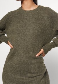 Neulepaita oliivinvihreänä, pyöreällä pääntiellä, väljällä istuvuudella ja resorireunuksilla hihoissa. Pehmeä rakenne ja rento siluetti.