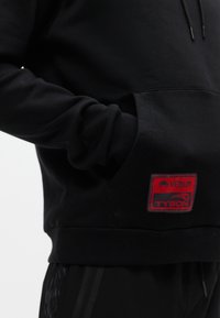 Μαύρο φούτερ με μαλακό ύφασμα και τσέπη καγκουρό, με κόκκινο λογότυπο Venum Tyson στο μπροστινό μέρος. Μακριά μανίκια και ριμπ τελείωμα.