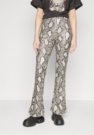 Pantalons évasés à imprimé serpent en beige, noir et blanc. Dotés d'une texture lisse et d'une taille haute, associés à des chaussures noires imposantes.