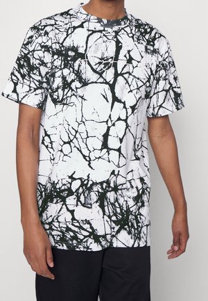 T-shirt blanc à manches courtes avec un motif abstrait noir en effet craquelé. Col rond. Le tissu semble lisse avec une légère texture.