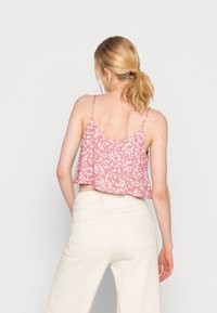 Top cropped rosa com padrão floral, com alças finas, corte solto e decote arredondado nas costas, combinado com calças beije de perna larga e cintura alta.
