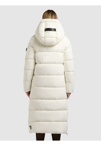 Ilgas pūkinis paltas kreminės spalvos, su erdvia kapišonu, horizontaliomis siūlėmis ir logotipo ženkleliu gale. Lygus, su izoliacija tekstūra.