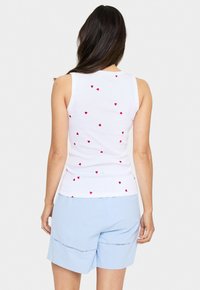 Top sin mangas blanco con pequeños patrones de corazones rojos, con un diseño ajustado y textura acanalada. Combinado con pantalones cortos azul claro.