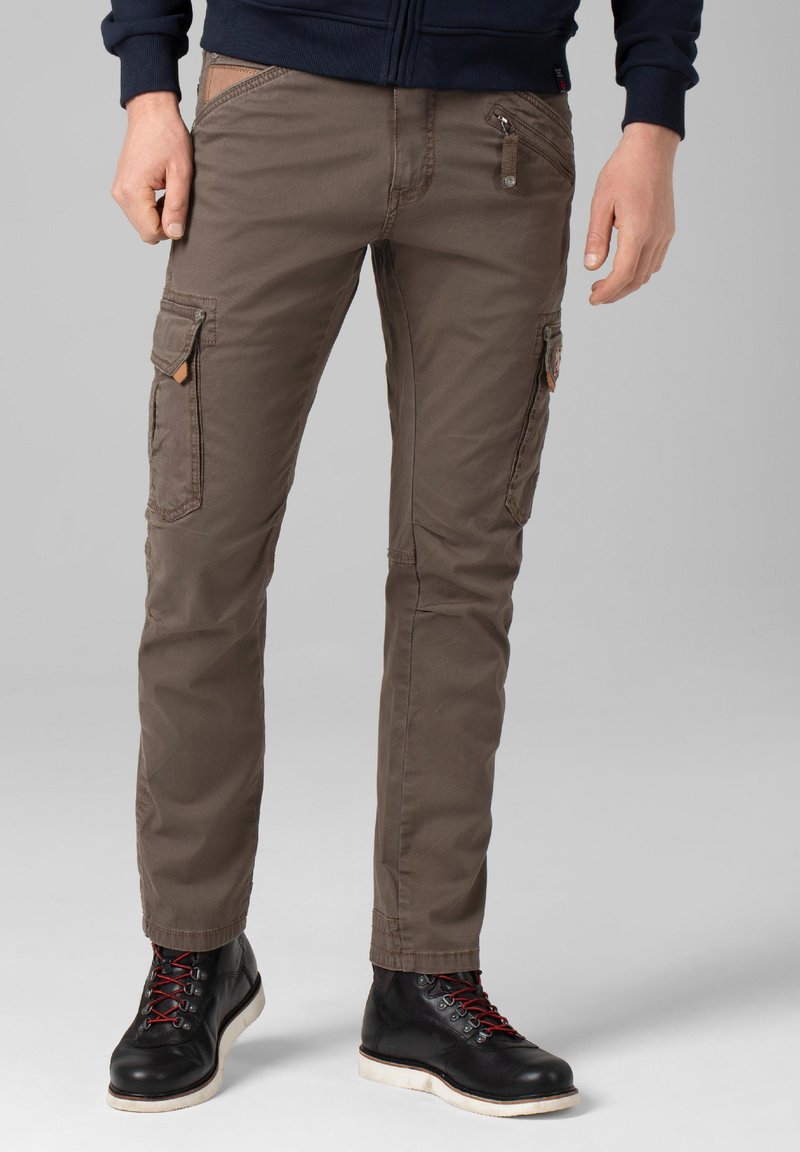 Cargo pants in earthy brown, featuring multiple pockets, a zipper closure, and a slim fit. Paired with black boots, showcasing red laces.