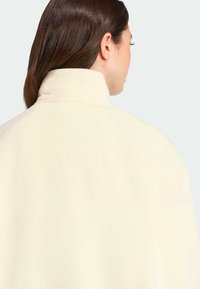 Veste en molleton couleur crème avec un col haut, présentant une texture lisse et une coupe décontractée, montrant la vue de dos.