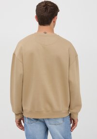 Felpa oversize beige con scollatura rotonda, spalle ribassate e polsini a coste. Realizzata in tessuto morbido con una texture liscia.