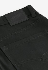 Zwart denim stof met een gestructureerde oppervlakte, voorzien van een gestikte zakontwerp en een merketiket. Accentueert door contrasterende stiksels.