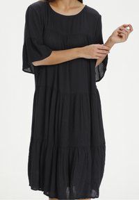 Robe noire à volants en tissu léger, avec un col rond et des manches à volant, présentant une silhouette fluide et une texture délicate.