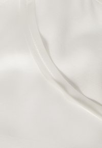 Primer plano de una tela blanca y suave con una costura curva y una textura sutil que muestra detalles de costura finos.