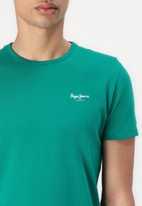 Green cotton T-shirt with short sleeves, round neck, featuring a white "Pepe Jeans London" logo on the left chest area.