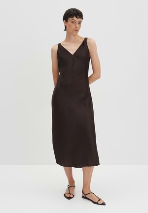 Dark brown, sleeveless dress with a V-neck, made of smooth fabric, falling to mid-calf. Paired with black strappy sandals.