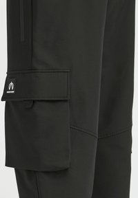 Svarte cargo-bukser laget av glatt stoff, med en sidelomme med klaff, sømdetaljer og en liten merkelapp.