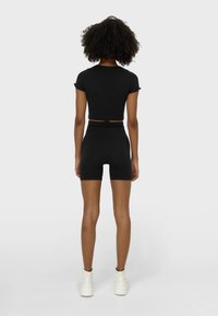 Zwarte cropped t-shirt gecombineerd met hoge zwarte shorts. Model draagt witte sneakers. Soepele textuur en slim-fit ontwerp.