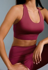 Reggiseno sportivo marsala con scollatura a profilo rotondo, design racerback e fascia elastica. Materiale liscio e elastico che si adatta al corpo.