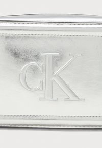 Metalický strieborný obal vyrobený z umelého kože, s embosovaným logom "CK". Koordinuje sa so štýlovým dizajnom a jemnou textúrou.