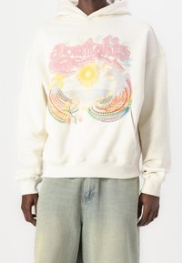 Felpa crema con un design grafico colorato che presenta un sole e fili arcobaleno. Tessuto morbido, vestibilità rilassata, polsini e orlo a costine.