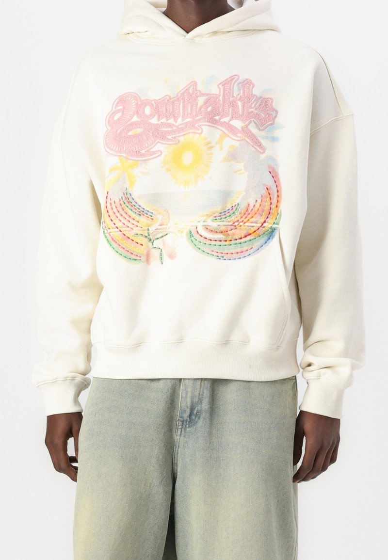 Felpa crema con un design grafico colorato che presenta un sole e fili arcobaleno. Tessuto morbido, vestibilità rilassata, polsini e orlo a costine.