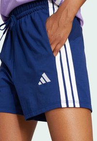 Mornarske šortse s bijelim trostrukim uzorkom duž bočnih strana. Tkanina je meka, s elastičnom tregom i malim izvezenim logotipom sprijeda.