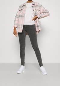 Camicia a quadri rosa e grigia sopra un felpa bianca, abbinata a jeans skinny grigi scuri e sneakers bianche. Tessuto morbido con dettagli in bottone.