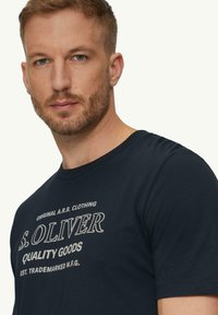 Navyblauwe T-shirt van katoen, met witte bedrukte tekst: "S. OLIVER QUALITY GOODS" en logo-details op de voorkant. Korte mouwen.