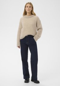 Beige mohair sweater med rund hals, ribbede manchetter og kant, parret med mørkeblå lige ben jeans og sorte sko.
