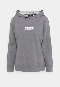 Felpa grigia con cappuccio regolabile, maniche lunghe e un'etichetta logo bianca con la scritta "CALVIN KLEIN" sul davanti. Tessuto morbido.