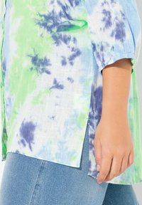 Camisa de botones en tejido ligero, con un patrón de tie-dye en verde, azul y púrpura. Incluye mangas fruncidas y aberturas laterales.