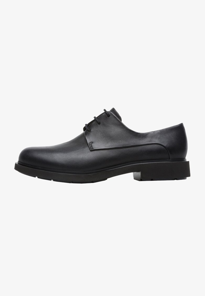 Chaussure habillée pour homme en cuir noir avec trois œillets pour lacets et un petit talon empilé, vue de côté sur un fond blanc.