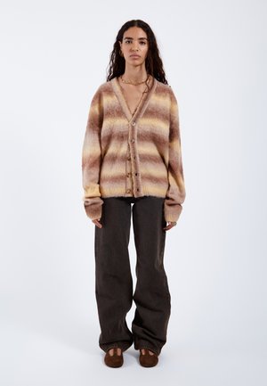 Brown and beige striped cardigan with a soft texture, V-neckline, and button closure. Paired with dark wide-leg pants and brown loafers.