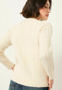 Cremfarbener Strickpullover mit strukturierten Mustern, gerippten Bündchen und Saum sowie einer taillierten Silhouette. Die Rückansicht zeigt das filigrane Design.