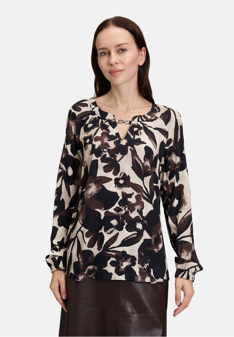 Long-sleeve blouse in a cream base with brown and black floral print. Features a v-neckline with a chain accent and gathered sleeves.