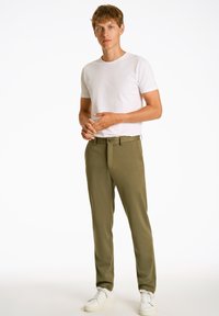 Olijfgroene broeken met een gladde textuur, rechte snit en riemlussen, gecombineerd met een aansluitend wit T-shirt met ronde hals en witte sneakers.