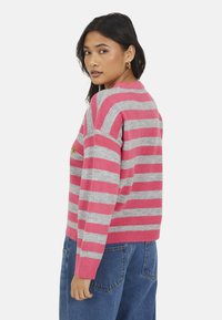 Pull rayé en rose et gris, avec un col rond, une coupe décontractée et une texture douce. Comprend un détail brodé sur le devant.