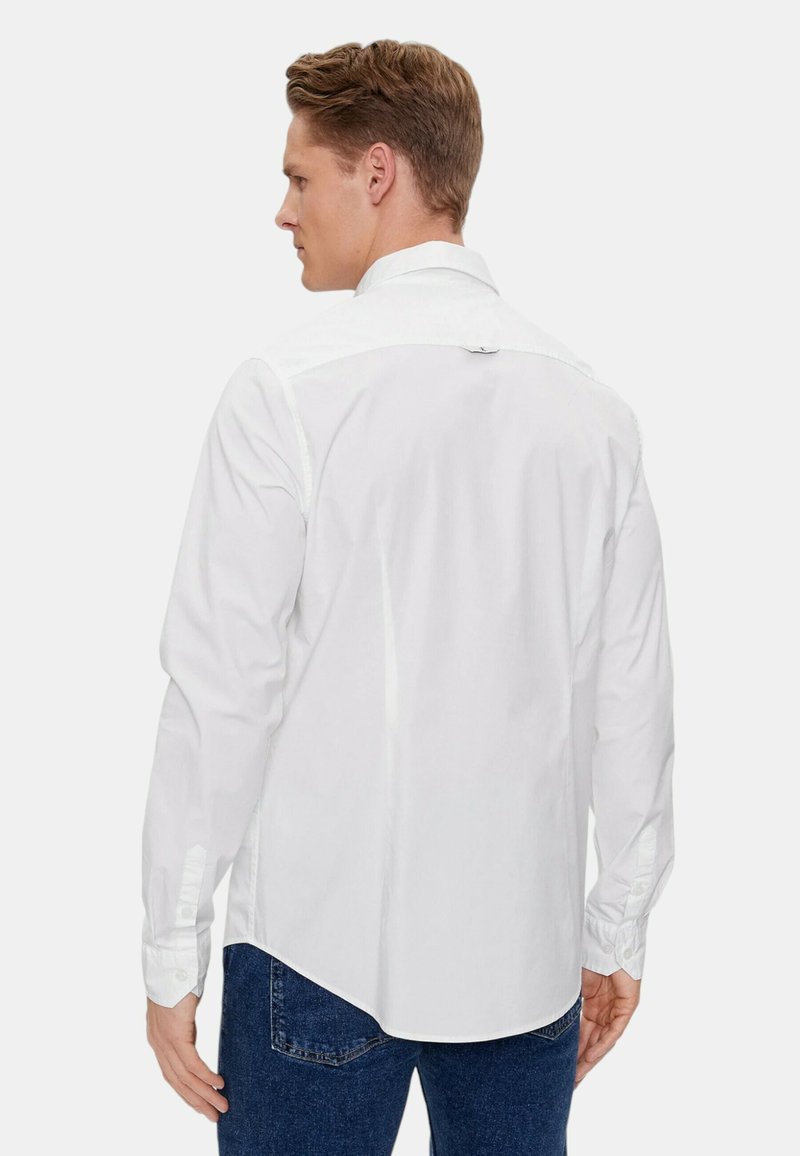 Biała, długosleznowa koszula z szpiczastym kołnierzykiem, gładką teksturą i zapinanymi mankietami. Z tyłu znajduje się przeszycie i lekko zaokrąglony dół.