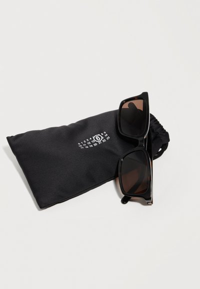 Μαύρα ορθογώνια γυαλιά ηλίου που ακουμπούν σε μια μαύρη θήκη με κορδόνι, με λευκούς αριθμούς τυπωμένους και λογότυπο 6 μέσα σε κύκλο.