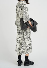 Lång, lös klänning med ett svartvitt abstrakt mönster, i kombination med en stor svart läderväska och svarta sandaler med remmar.