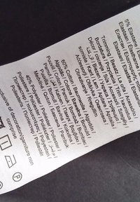 Hoito-ohjeet useilla kielillä, jossa kerrotaan materiaalit: 60 % puuvillaa, 40 % polyesteria ja 5 % elastaania, valkoisella taustalla.