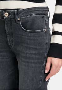 Jean en denim noir à coupe slim, comprenant cinq poches, avec un léger effet délavé et des accents de couture contrastés le long des coutures.