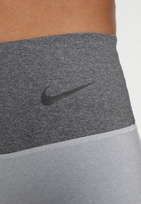 Szare i jasnoszare legginsy do ćwiczeń o gładkiej teksturze, z czarnym logo Nike na pasie i kontrastującymi kolorowymi sekcjami.