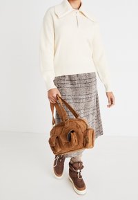 Pull en maille beige à col montant, jupe écossaise marron et sac en velours côtelé marron. La tenue comprend des bottes marron lacées et des détails en tissu texturé.