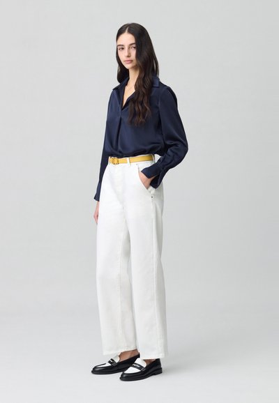 Blusa de satén azul marino con cuello, pantalones de pierna ancha blancos con bolsillos, cinturón amarillo y mocasines negros con acentos blancos.
