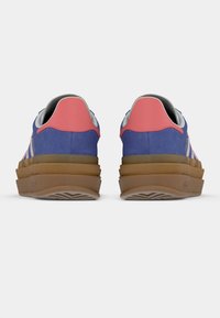 Par blå og rosa sneakers med tykk brun såle sett bakfra på hvit bakgrunn.