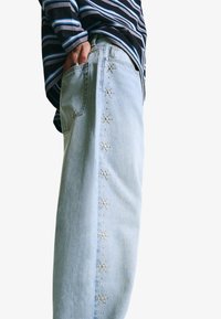 Ljust blå denimjeans med dekorativa pärlliknande detaljer längs sömmen, tillsammans med en mörk randig topp.