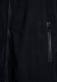 Veste en polaire noire avec fermeture éclair à l'avant et poche zippée, présentant une texture douce et une finition lisse.