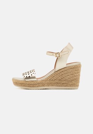 Sandalias de cuña con parte superior metálica dorada y correa perforada, que cuentan con una plataforma de yute trenzado y suela texturizada. Correa ajustable en el tobillo.