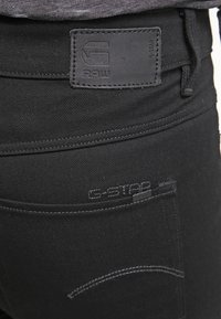 Jean en denim noir avec une étiquette en cuir G-Star RAW et des détails cousus. Comprend une poche arrière avec un logo de marque subtil et une texture lisse.